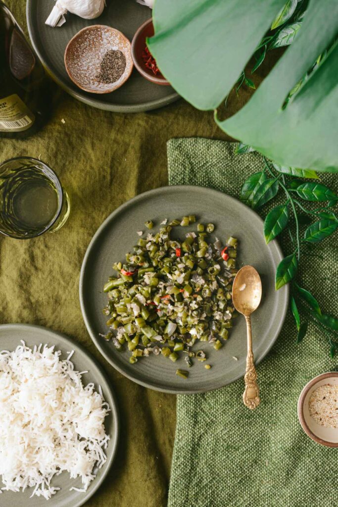 This is a picture of green beans poriyal on a plate along with cooked basmati rice set on a table