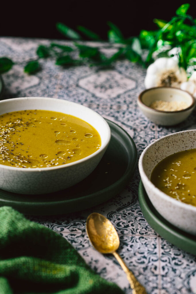 This is a picture of okra lentil soup in 2 bowls along with sesame seeds in a small bowl in the background.