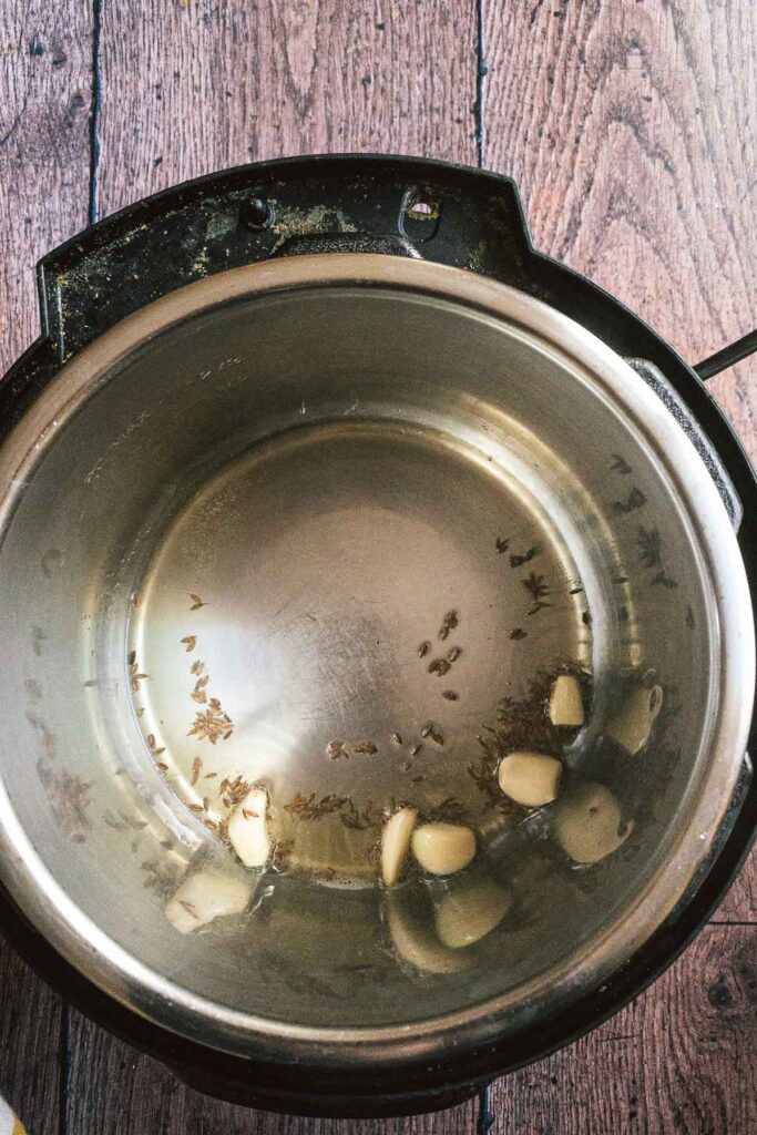 Picture of cumin seeds and garlic cloves added to the instant pot.