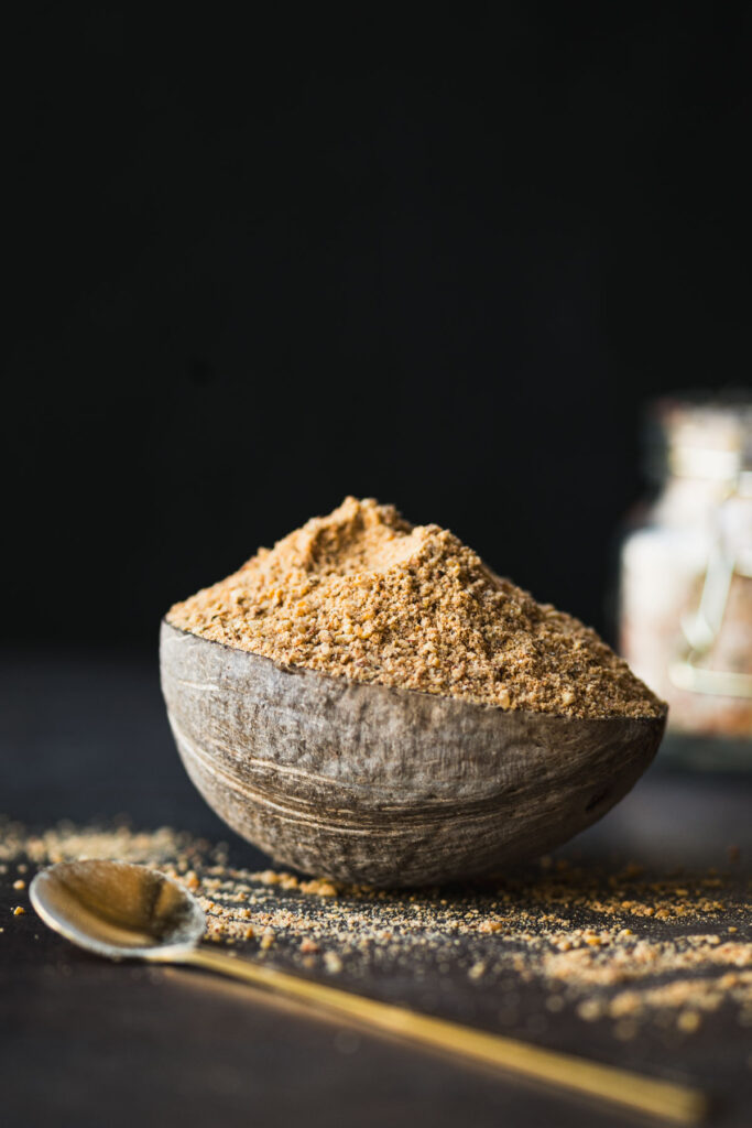 This is a picture of Idli Podi in a coconut bowl kept on a table along with a spoon