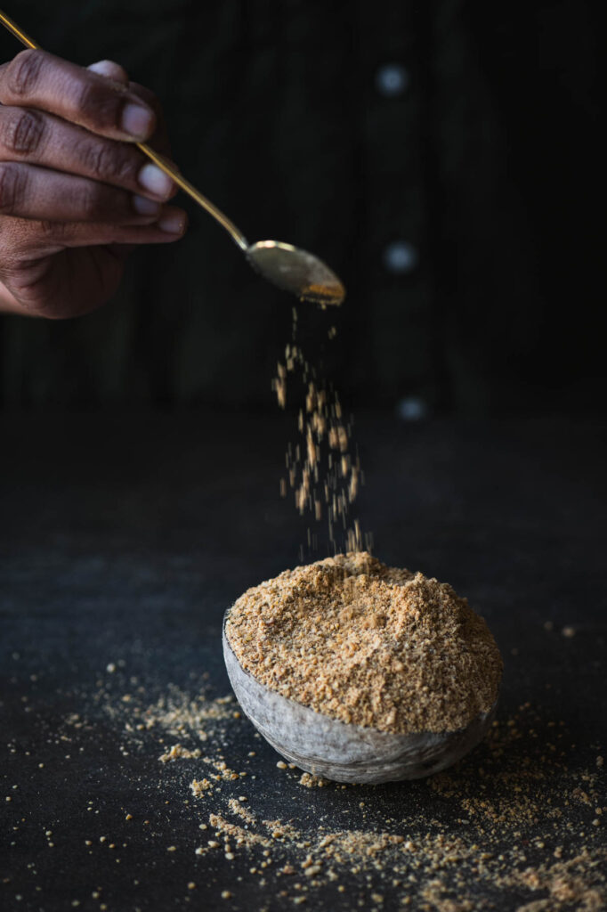 This is a picture of a girl sprinkling some idli dosa posi onto a bowl with a spoon