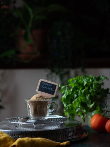 This is a picture of rasam powder blend on a cup of glass on a table .