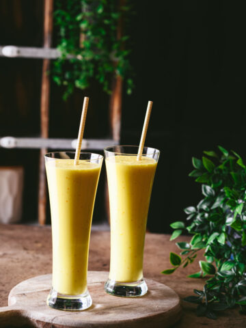 This is a picture of 2 glasses of saffron pistachio lassi on the table.