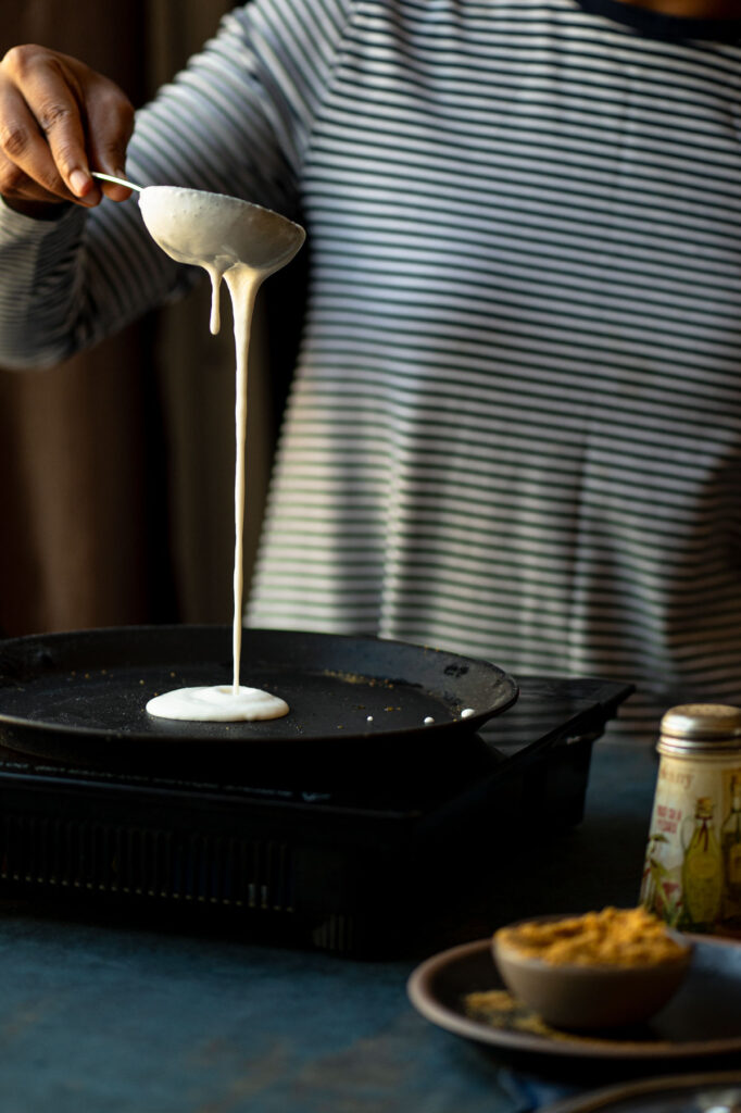 Pouring a ladle of dosa batter to make gun powder dosa