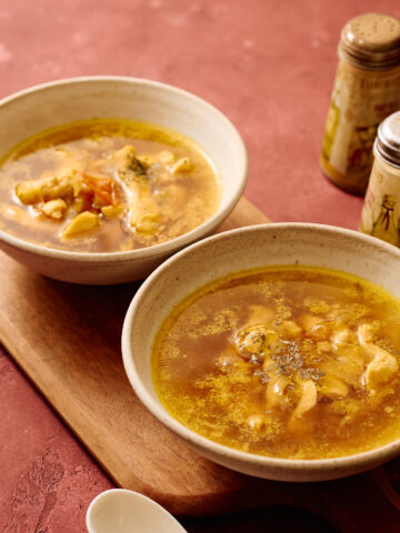 Instant Pot Indian chicken soup served in ceramic bowls, light golden broth with tender chicken, photographed in a warm, rustic setting.